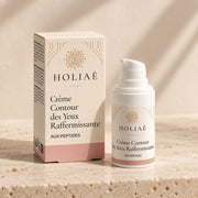 Crème Contour des Yeux Raffermissante aux Peptides HOLIAĒ avec pot et étui sur fond ivoire