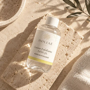 Lotion Exfoliante à l’Acide Glycolique AHA 5 % HOLIAĒ en mise en scène éditoriale sur travertin