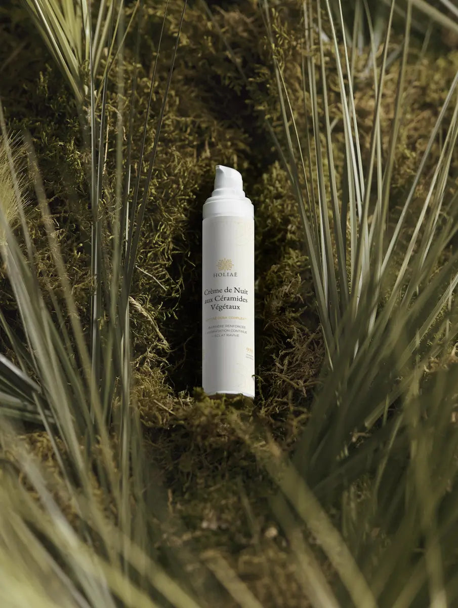 Flacon de crème de nuit anti âge Holiaē posé dans un décor végétal naturel, ambiance soin biomimétique.