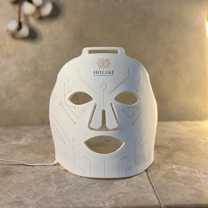 Masque LED visage Holiaē RĒ:GEN I — packshot debout, circuits dorés sur fond minéral.